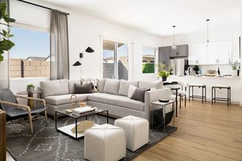 A modern living room with a grey sofa, a glass coffee table, and a black chair.